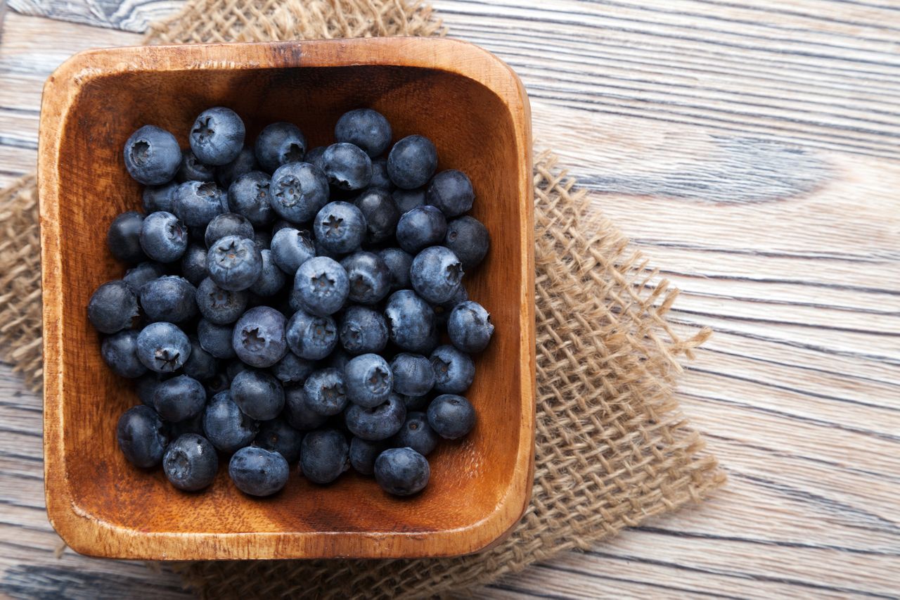 A bowl of blueberries on a wooden and burlap surface.