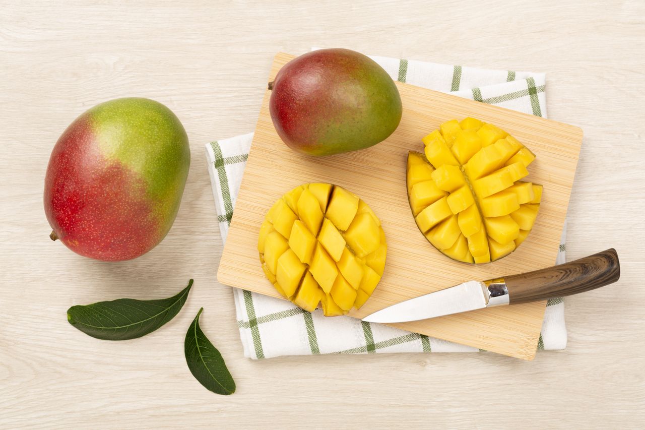 Sliced mangoes and whole mangoes on a cutting board with a knife.