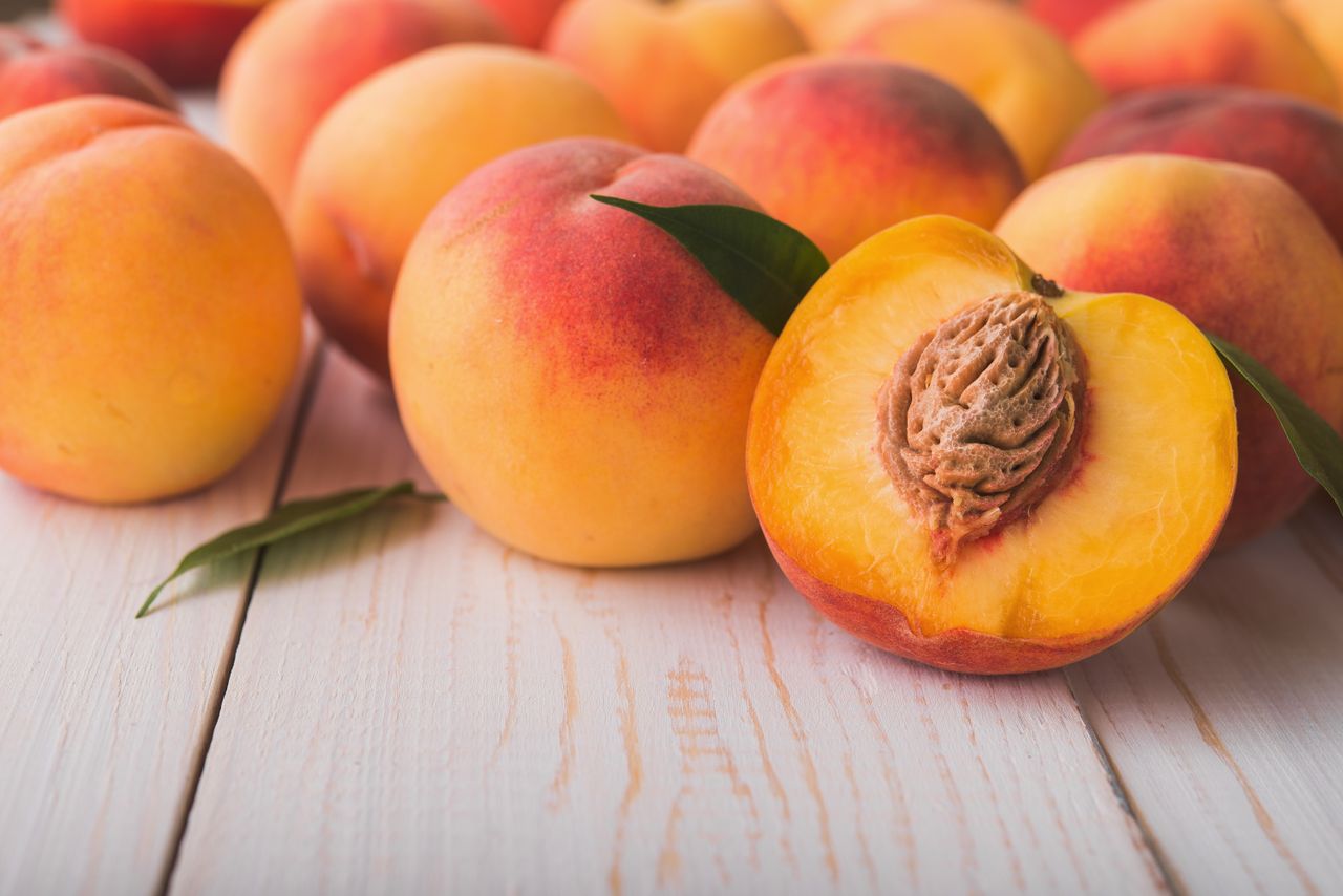 Fresh peaches on a wooden surface, with one sliced to reveal the pit.