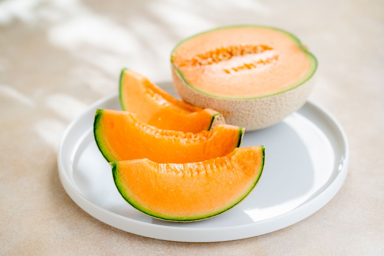 A halved cantaloupe and three melon slices on a plate.