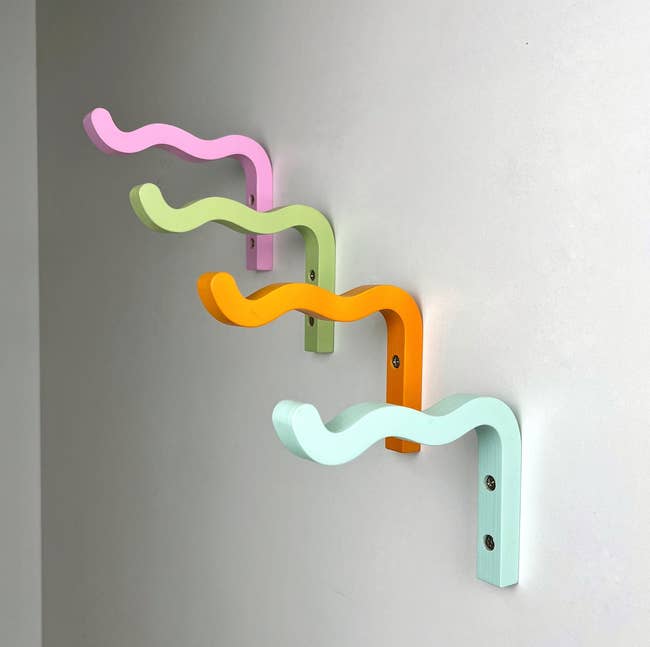 Wall-mounted wavy hooks in pastel colors displayed in a row, used for organizing or hanging items