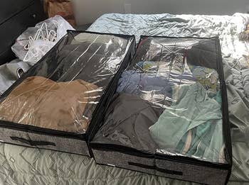 Two storage bags on a bed, filled with neatly folded clothes, demonstrating organized storage solutions. A dog is lying nearby