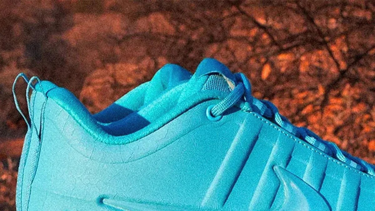 Close-up of a bright blue sneaker with textured upper and laces, set against a blurred brown outdoor background.