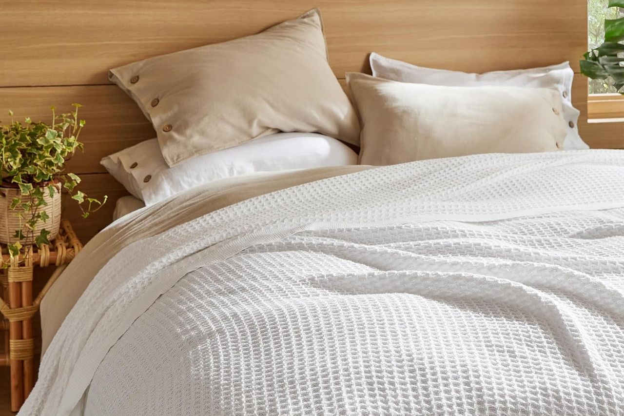 A neatly made bed with white textured bedding beige pillows and plants on bedside decorations