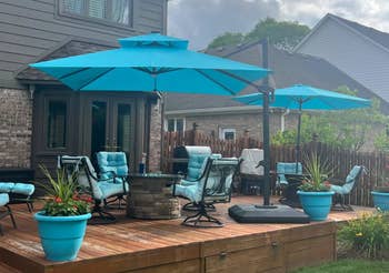 Patio with cushioned chairs, umbrellas, and potted plants on a wooden deck attached to a brick house