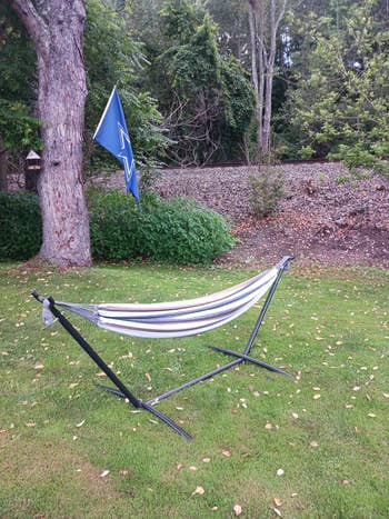 Outdoor hammock with a striped fabric on a metal stand, set on a grassy lawn near trees and a flag