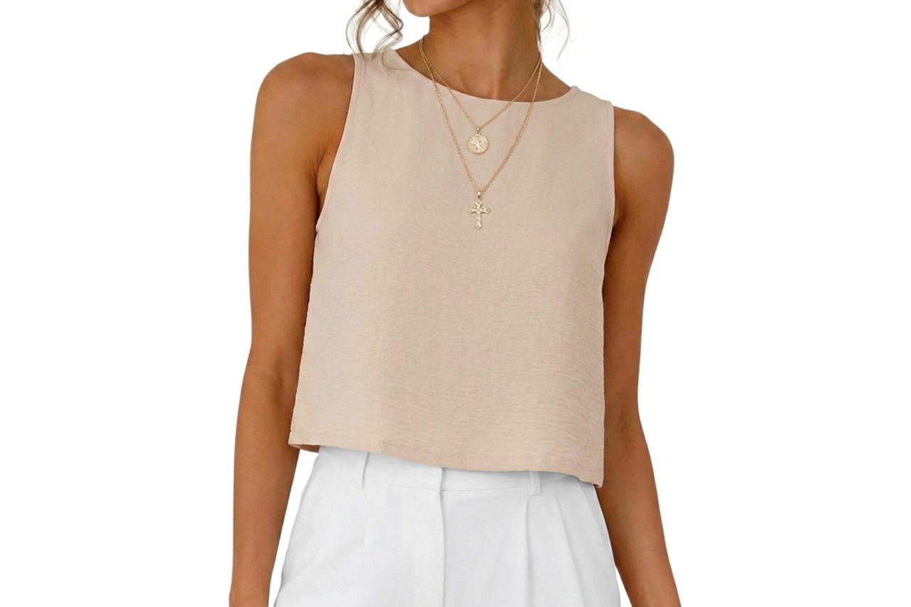 A woman wearing a sleeveless crop top and white pants shown from the neck down