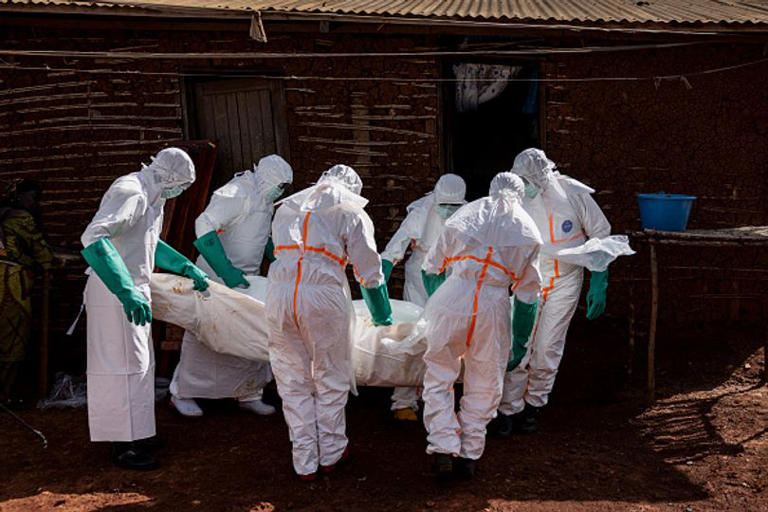 MONGBWALU, DEMOCRATIC REPUBLIC OF CONGO - MAY 24: Health workers wearing protective equipment carry the body of a suspected Ebola victim during safe burial procedures outside a family home in the community of Mongbwaluon on May 24