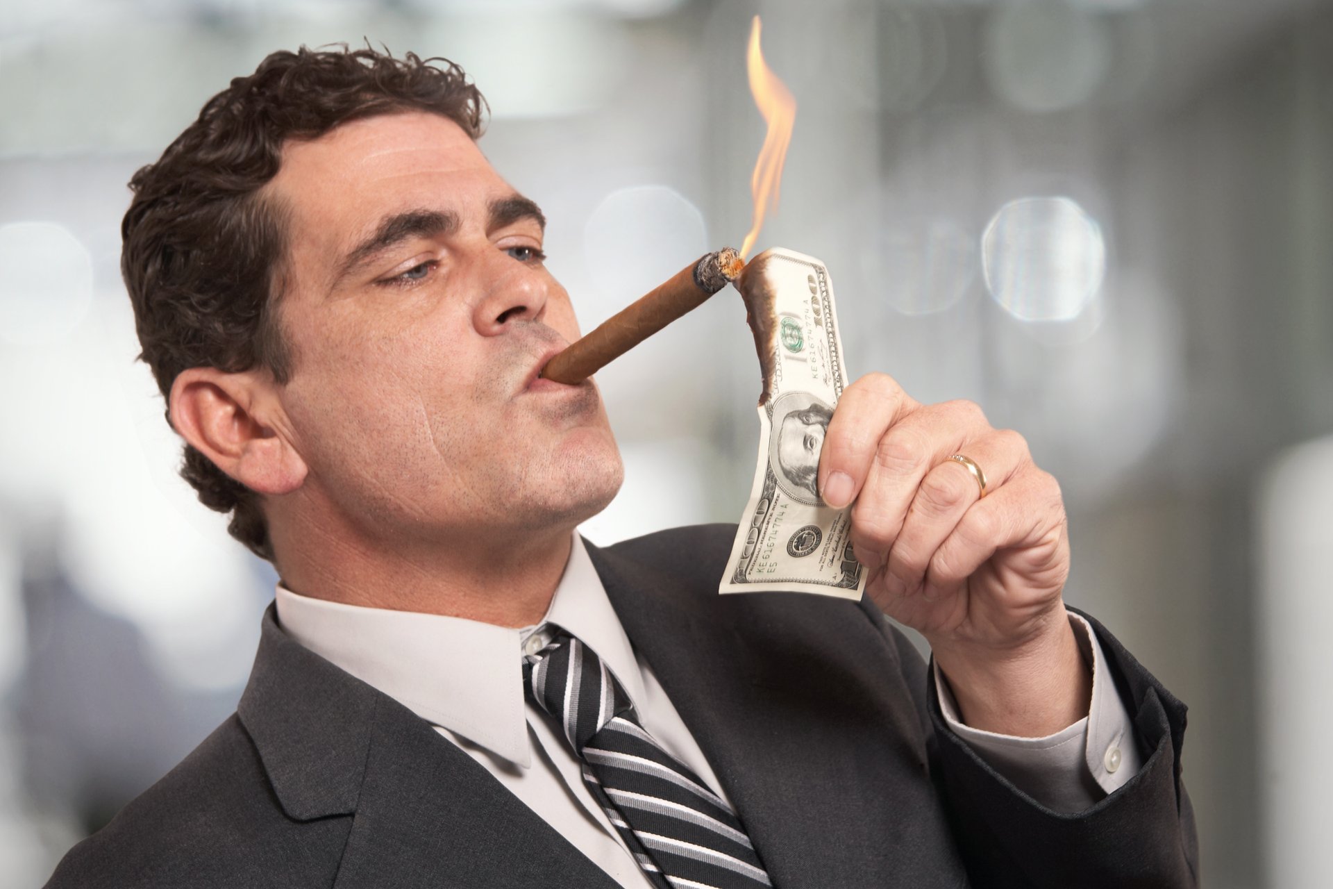 Rich guy lighting cigar with money.