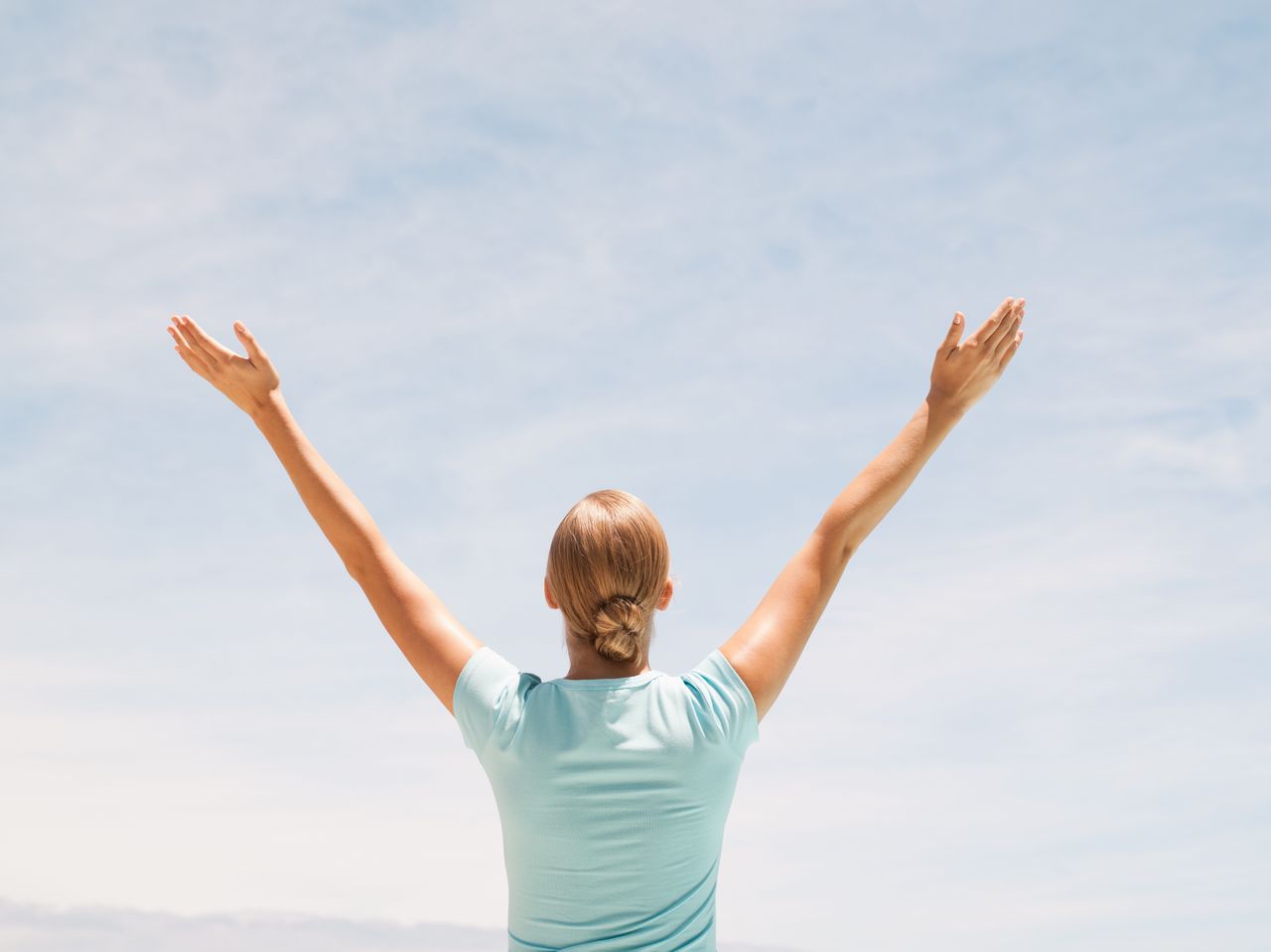 A blonde woman facing away from the camera has her arms up in a
