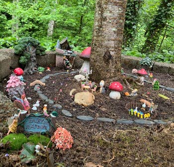 Fairy garden with small houses, figurines, and toadstools nestled around a tree in a natural setting