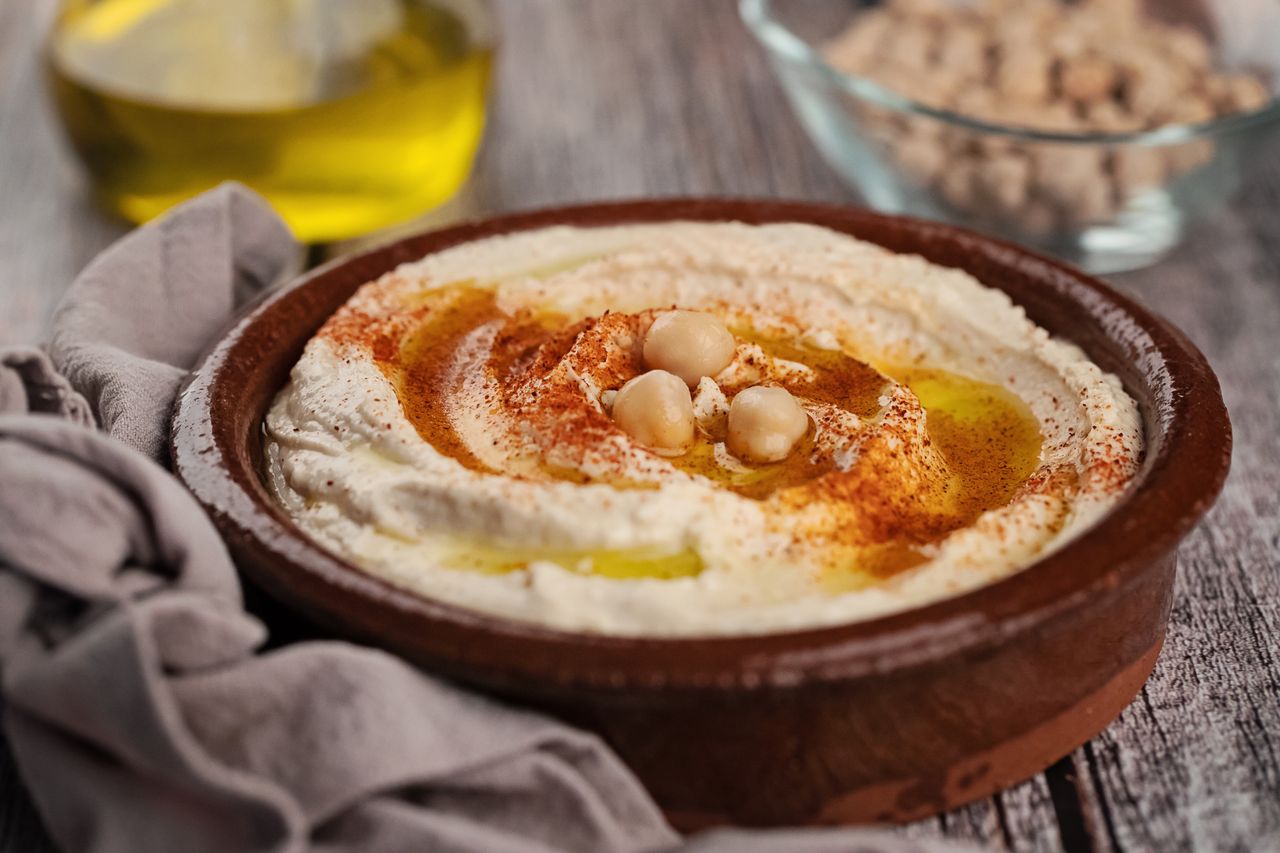Plate of hummus topped with olive oil chickpeas and paprika on a wooden table