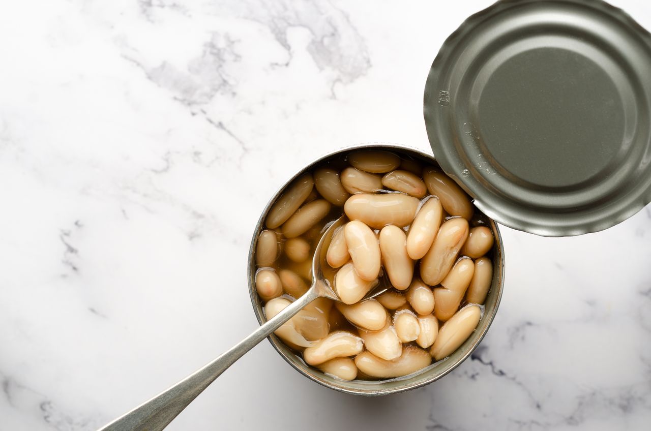 An opened tin of white beans with a spoon resting inside