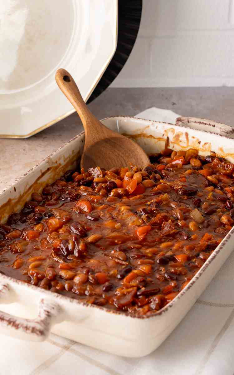 A serving spoon stuck in a dish of homemade baked beans.