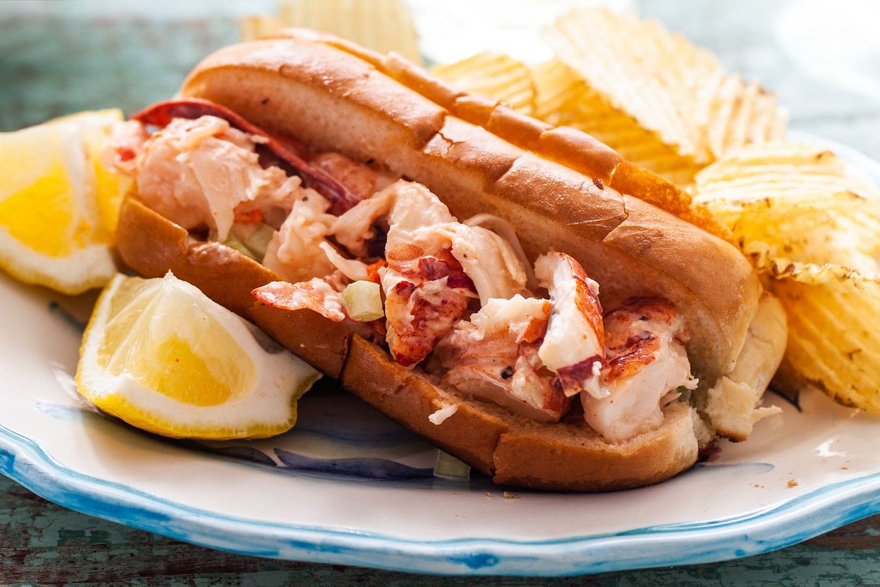 Lobster roll on a plate with chips and a lemon wedge
