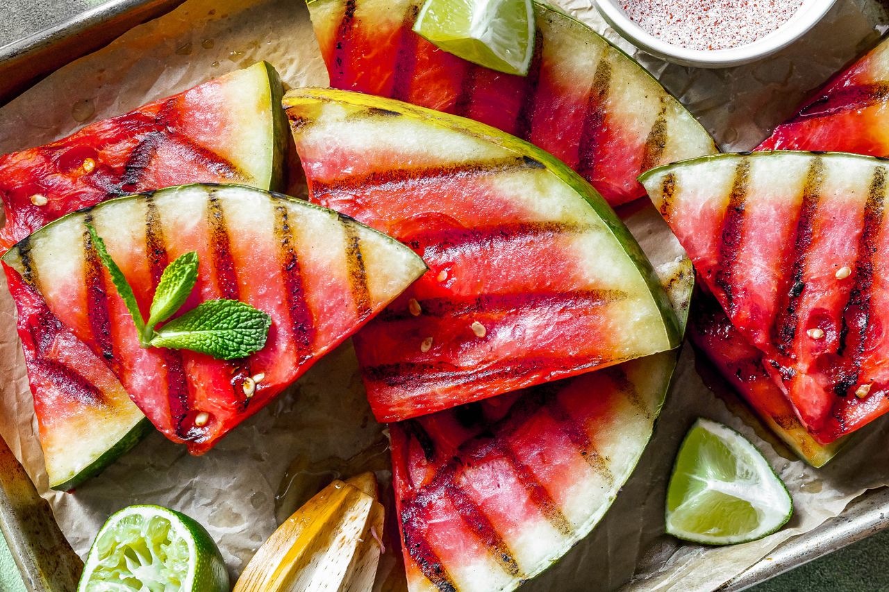 Triangles of grilled watermelon with small bowl of spice mix, sprig of mint and lime wedges alongside