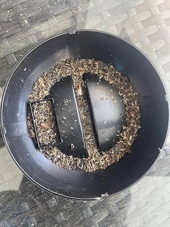 Close-up of birdseed remnants in a large black bowl placed on a wicker surface, possibly after being used to feed birds