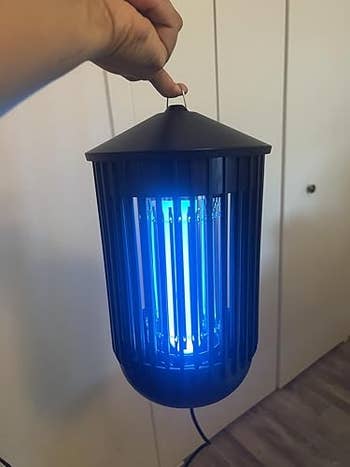 A hand holding a portable bug zapper with glowing blue light, suitable for indoor or outdoor use