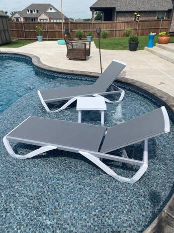 Two sleek poolside loungers with a small table between them, placed on a mosaic-tiled pool ledge, creating a luxurious relaxation spot