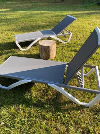 Two outdoor lounge chairs on grass with a small wooden stump table between them