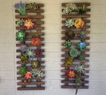 Two wooden vertical planters on a brick wall hold a variety of succulents and air plants in a neat arrangement under an outdoor light fixture