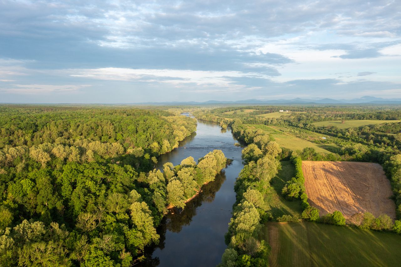 Aerial view of a river flowing through a forested and agricultural landscape under a cloudy sky