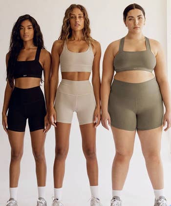 Three models stand in athletic wear consisting of sports bras and shorts, showcasing different body types, promoting inclusive activewear