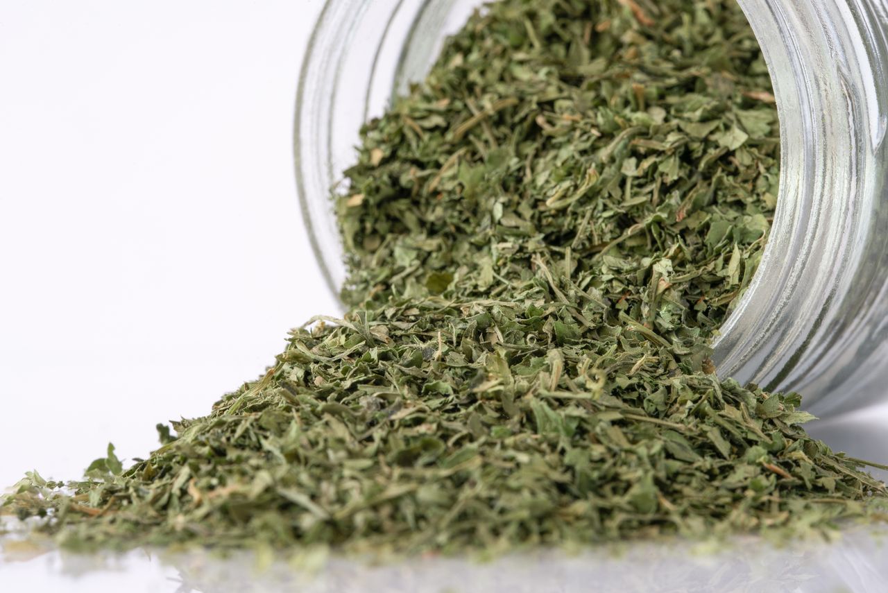 Dried green herb spilling from a glass jar onto a tabletop