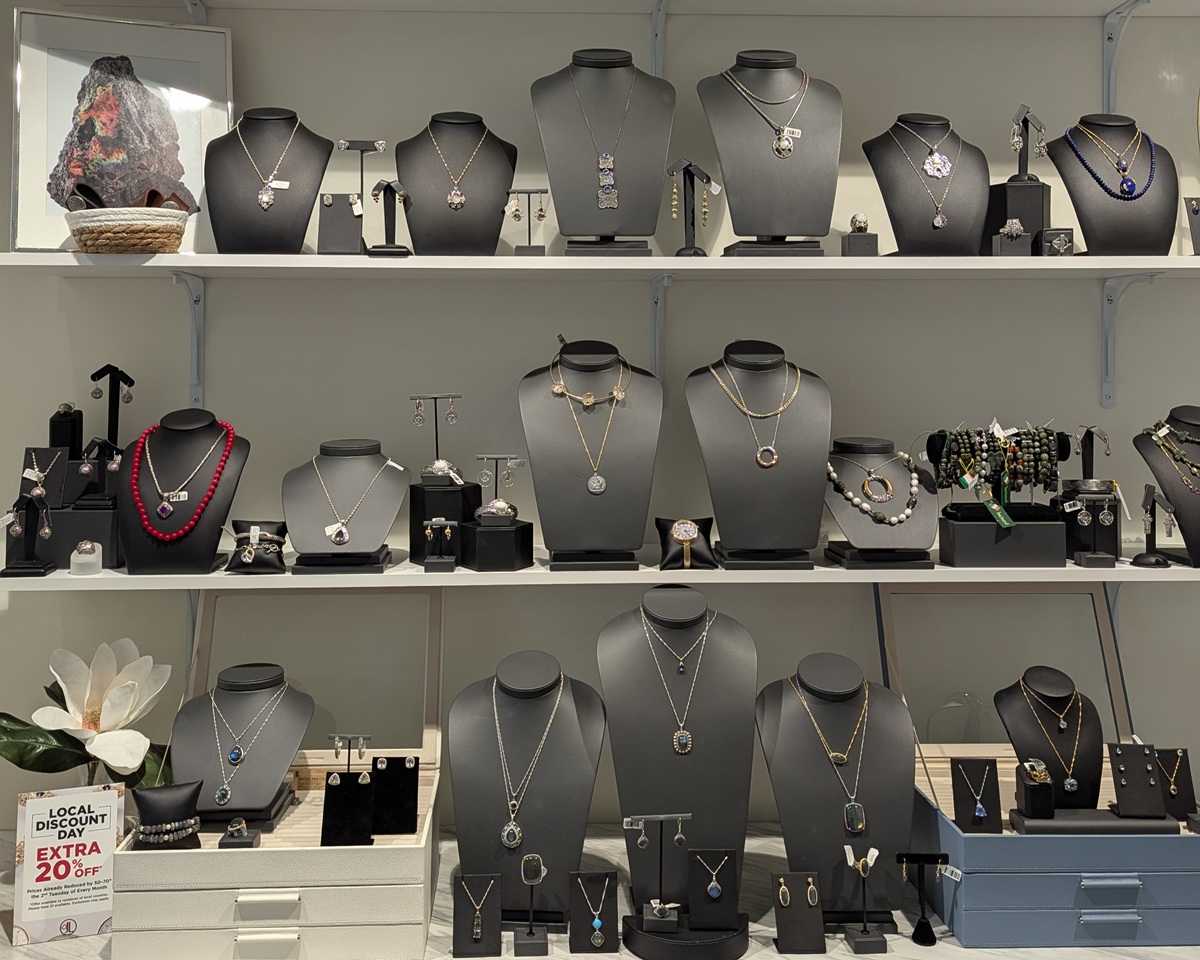 White retail shelves display rows of necklaces, bracelets, rings, and earrings on black jewelry busts and stands, creating a neat boutique style arrangement at Jewelry Love by JTV at The Mountain Mile in Pigeon Forge, Tennessee. A small sign reads