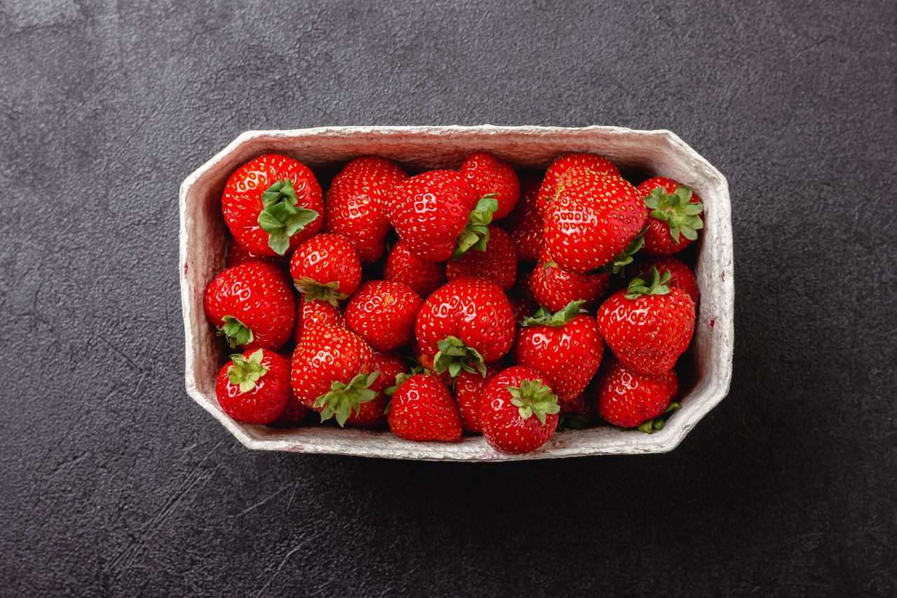 A basket of fresh strawberries on a dark surface.