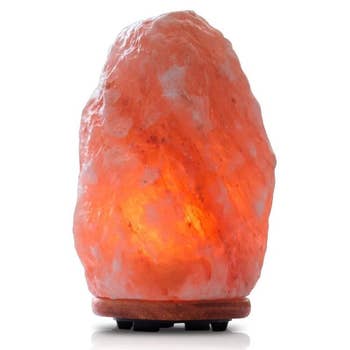 Himalayan salt lamp on a wooden base, glowing softly. Featured in a Shopping article