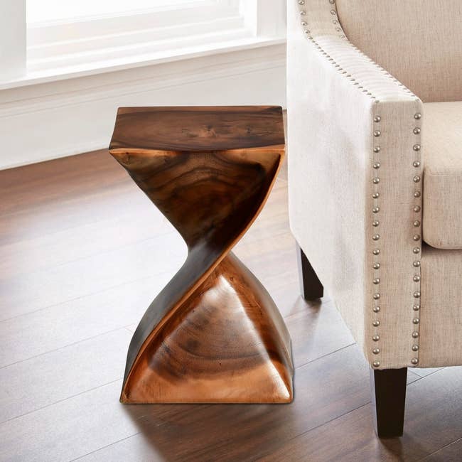 Sculptural wooden side table with twisted design beside a studded armchair in a bright room