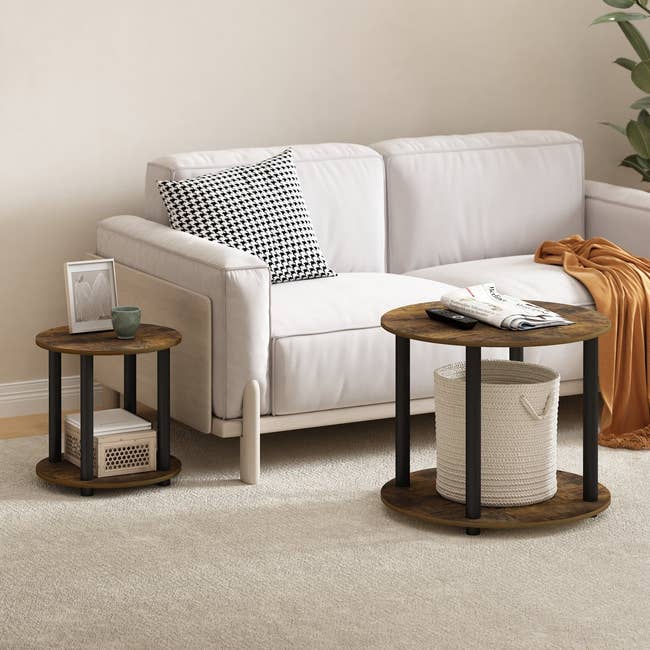 Living room with a white sofa, two round wood tables, houndstooth pillow, plant, magazine, and basket. Neutral decor for a cozy setting