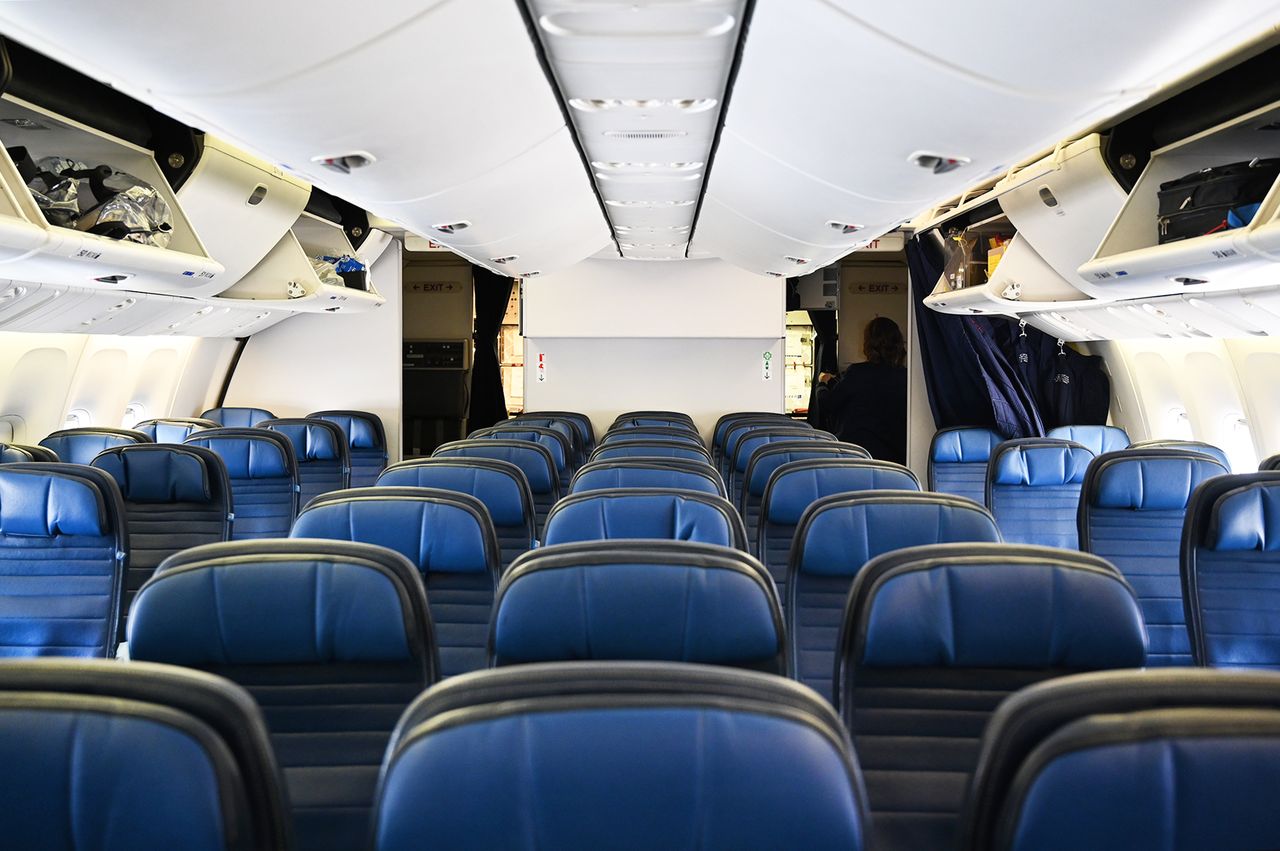 View of a passenger airplane cabin looking toward the cockpit rows of blue seats along an aisle