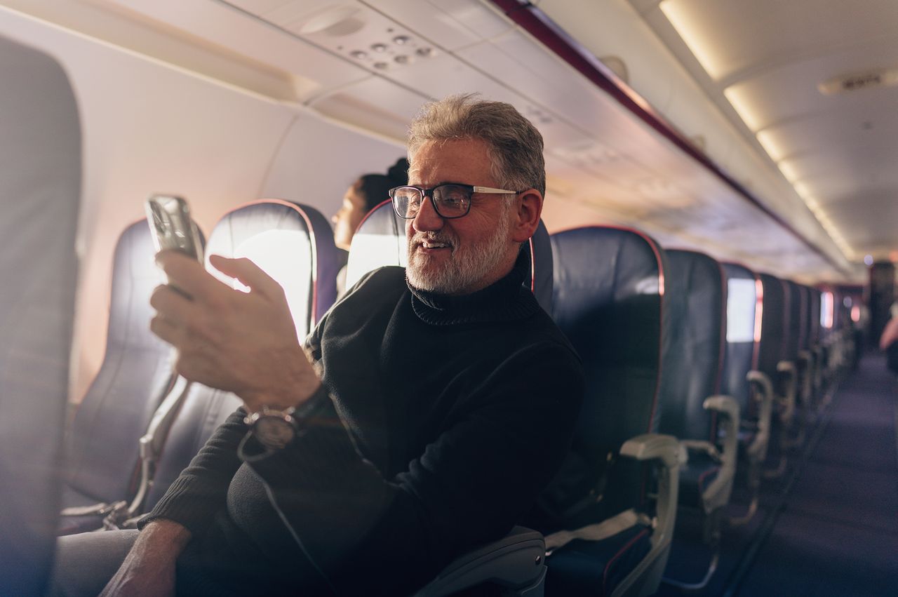 A man seated on an airplane holding a smartphone empty seats around him