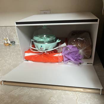 Bread box with bread, an egg cooker, and a bag behind a flap