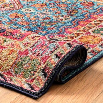 Decorative rug with intricate patterns, partially rolled up on a wooden floor