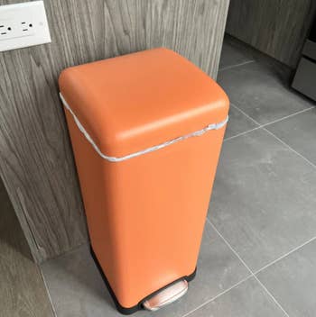 Orange rectangular trash bin with a foot pedal in a modern kitchen setting