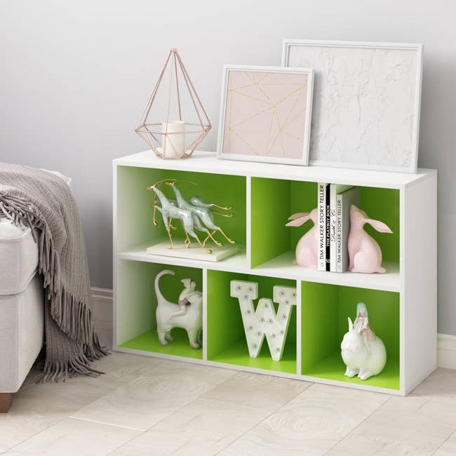 Decorative shelf with green compartments displaying decorative items like books, animal figurines, and framed art, beside a light couch