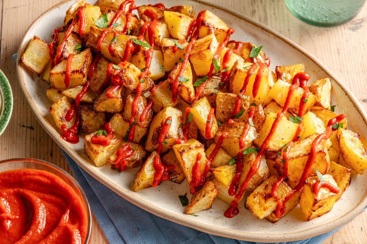 Angled view of a platter of roasted diced potatoes and topped with tomato sauce and parsley all on a wooden table top