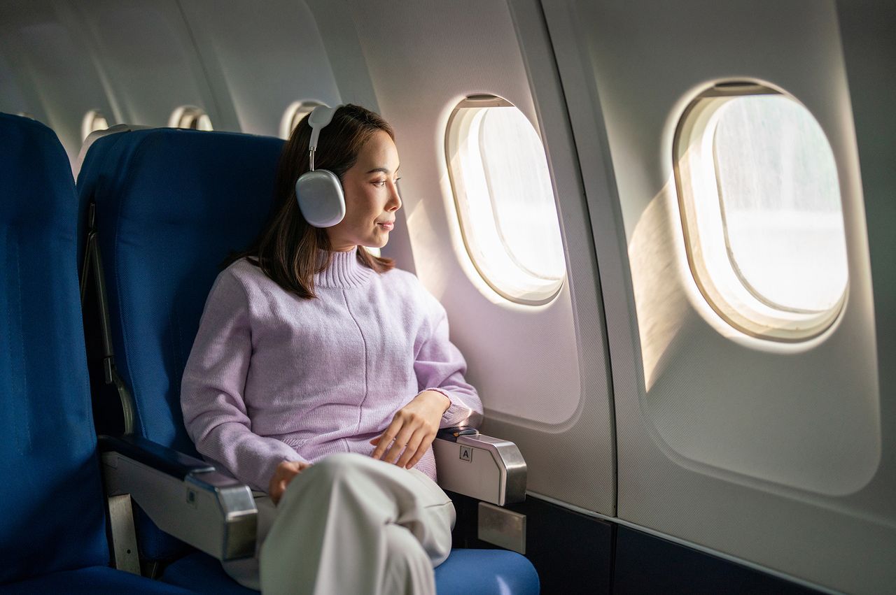 A passenger wearing headphones seated by an airplane window