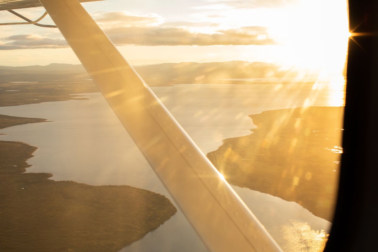View from an aircraft window showing a coastline and water bodies illuminated by the sunlight