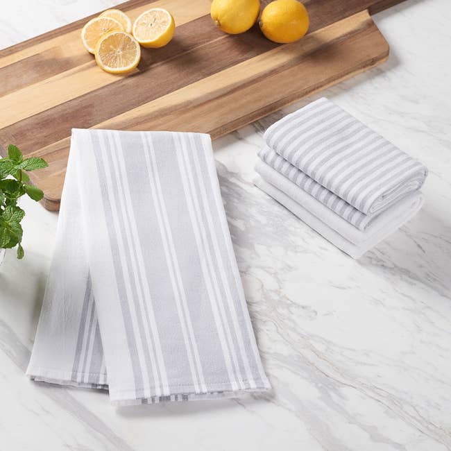 Striped kitchen towels displayed on a marble surface with lemons, a mint sprig, and a wooden cutting board