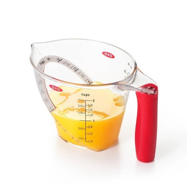 Measuring cup with red handle, marked in cups and milliliters, holds liquid up to 2/3 cup