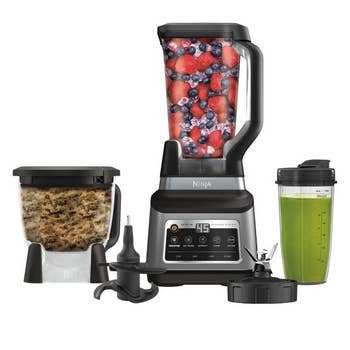 Ninja blender system with three attachments shown: blending pitcher filled with berries, food processor with dough, and smoothie cup with green drink