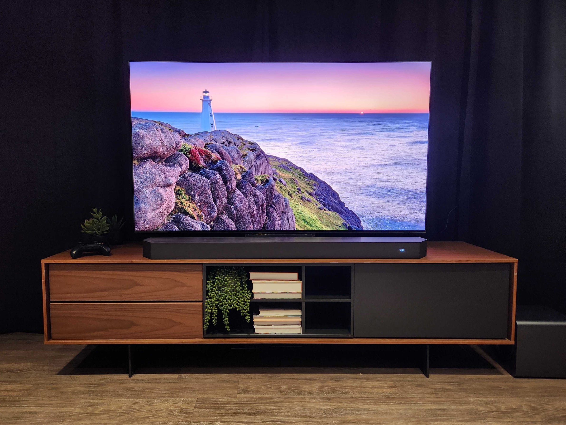 A Samsung R95H Micro RGB TV on a media console with an image of a lighthouse overlooking an ocean on its screen.