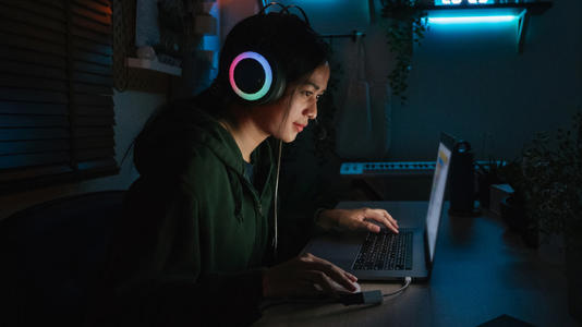 A woman playing a video game on a laptop with flashy headphones on