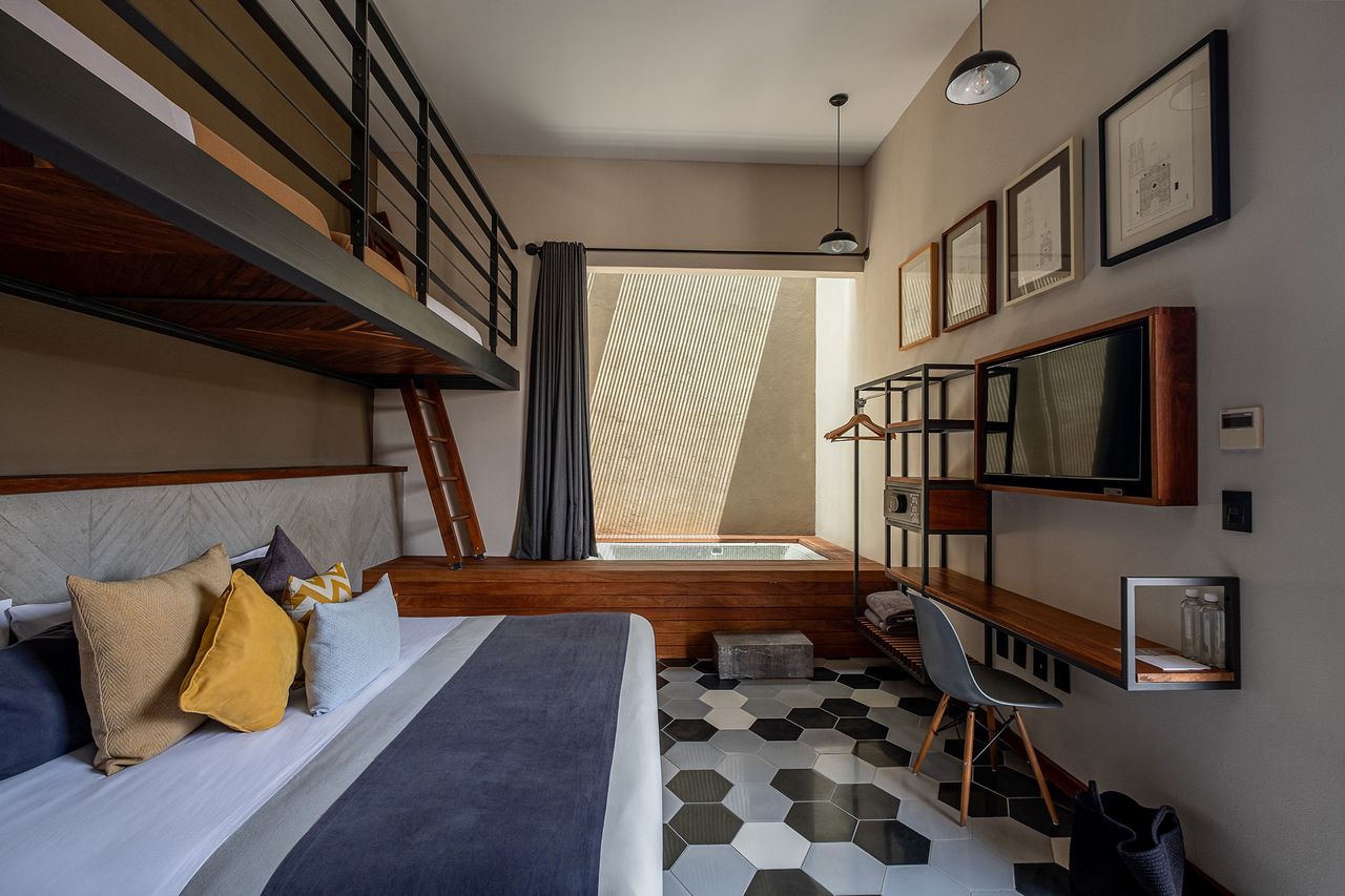 A modern hotel room interior with a bed loft area desk and framed artwork on the walls