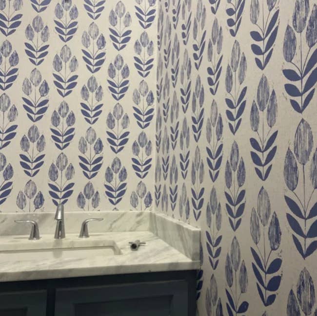 Bathroom sink area with a marble countertop and floral-patterned wallpaper. This image is part of a Shopping article showcasing decor ideas