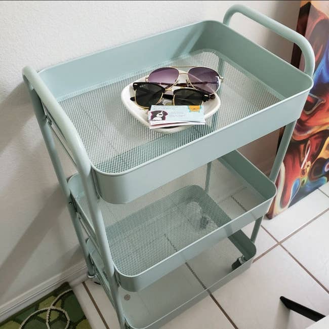 A three-tier rolling cart with sunglasses and accessories on top, ideal for stylish home organization and storage solutions